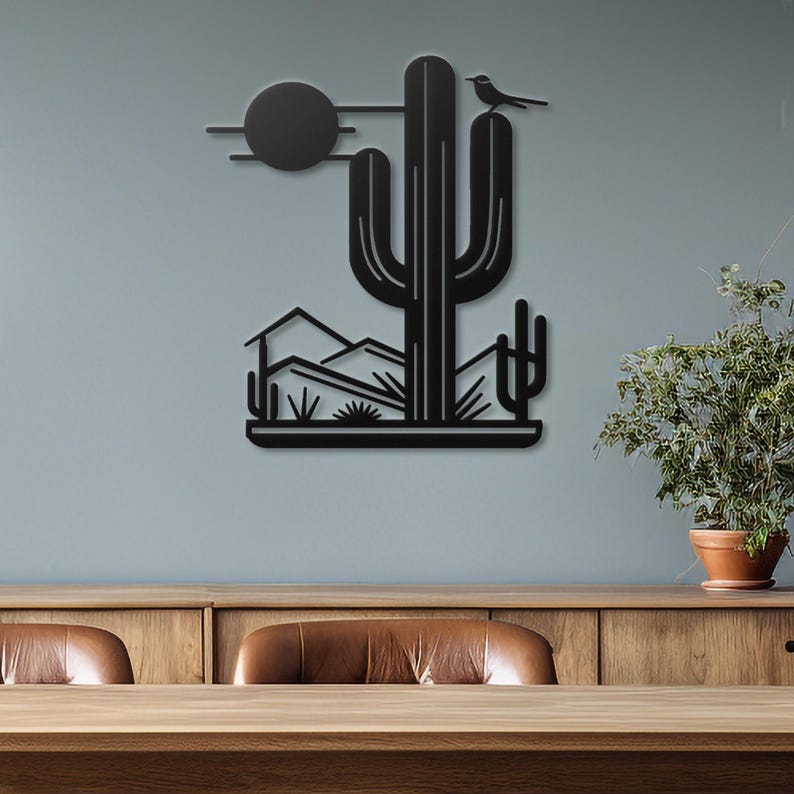 May include: Black metal wall art depicting a desert landscape with a large cactus, smaller cacti, mountains, and a bird perched on the cactus. The art is mounted on a light grey wall.