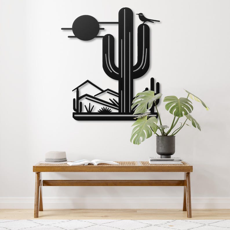 May include: Black metal wall art depicting a desert landscape with a cactus, mountains, and a sun. The cactus has a bird perched on top.