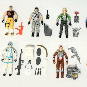 May include: A selection of vintage action figures, each with distinct outfits and accessories. The figures are in various colours, including green, blue, yellow, and grey. Accessories include weapons, communication devices, and backpacks.