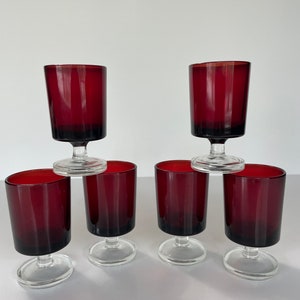 May include: Set of six red glass stemmed shot glasses. The glasses are stacked in a pyramid shape.