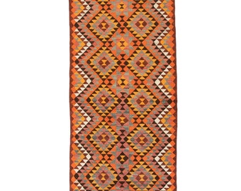 May include: A long, narrow rug with a geometric pattern in shades of orange, brown, gray, and white. The pattern is made up of triangles and diamonds.