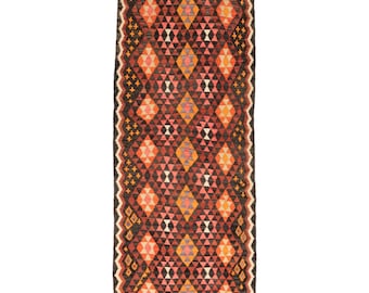 May include: A long, narrow rug with a geometric pattern in shades of red, orange, pink, and black. The rug has a traditional, hand-woven look.
