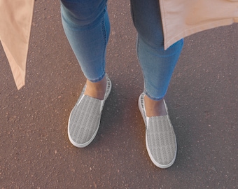 May include: A pair of black and white slip-on shoes with a chevron pattern. The shoes are worn by a person wearing blue jeans.