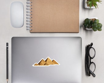 May include: A sticker featuring a photograph of the Great Pyramids of Giza in Egypt. The pyramids are a light brown color and are set against a blue sky.