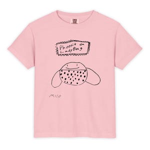 May include: A light pink t-shirt featuring a hand-drawn ladybug design. The ladybug has a dotted pattern and is accompanied by the text "Phoenix da LadyBug" in a rectangular frame. The artist's signature, "milo," is at the bottom.