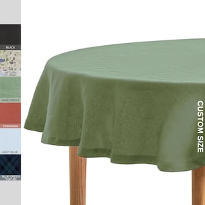 May include: Sage green round tablecloth with a custom size option. The tablecloth is draped over a wooden table.