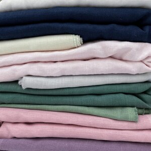 May include: A stack of fabric swatches in various colors, including white, pink, green, purple, and blue. The fabric appears to be linen or a similar natural fiber.