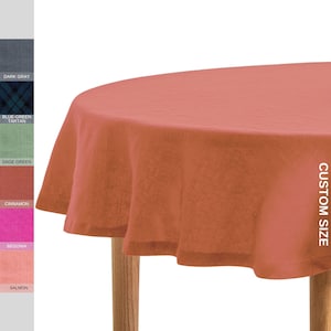 May include: A round, salmon-coloured tablecloth draped over a wooden table. The tablecloth has a custom size and is made of linen.