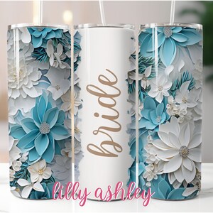 May include: A white stainless steel tumbler with a blue and white floral design and the word "bride" in gold lettering. The text "lilly ashley" is at the bottom of the tumbler.