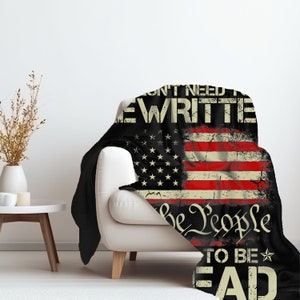 May include: A black and red fleece blanket with a distressed American flag design. The text "We don't need to be rewritten, We the People, to be read" is printed on the blanket.