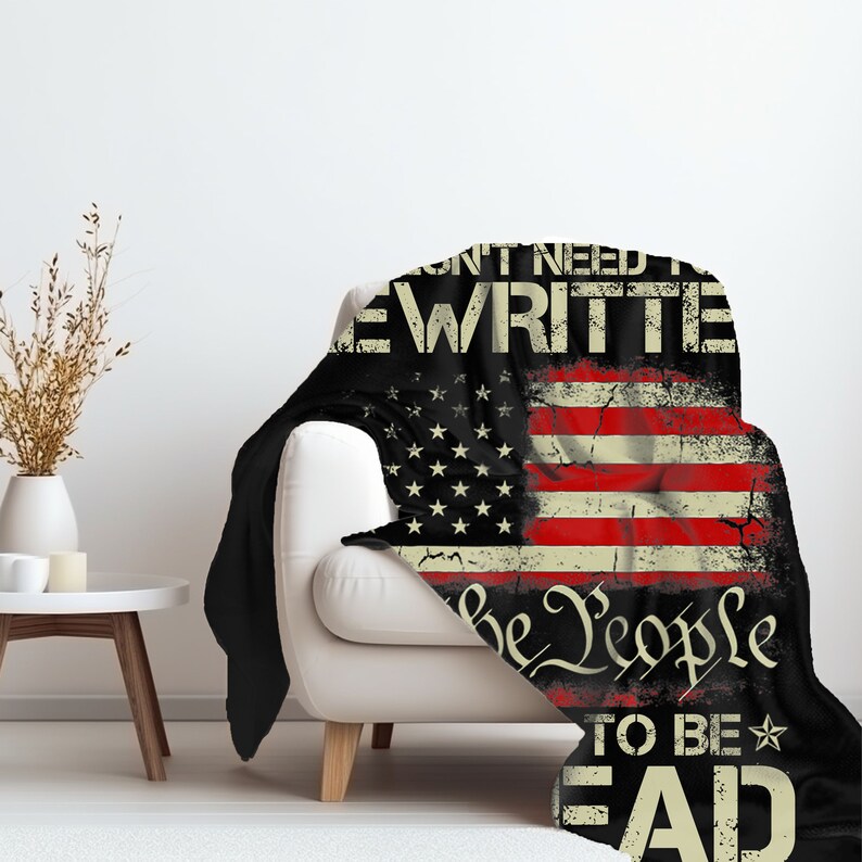 May include: A black and red fleece blanket with a distressed American flag design. The text "We don't need to be rewritten, We the People, to be read" is printed on the blanket.