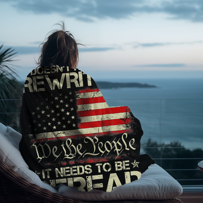 May include: A black and red blanket with an American flag design. The blanket has the text "Doesn't get rewritten" and "We the People" with a star and the text "It needs to be read" on it.