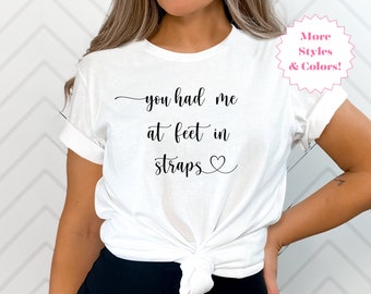 May include: White t-shirt with the text "you had me at feet in straps" and a small heart symbol.