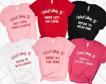 May include: Six pink, red, and black t-shirts with white text that reads "Most Likely To" followed by a different phrase on each shirt. The phrases are "Buy Their Own Flowers", "Swipe Left On Cupid", "Refuse To Wear Pink", "Show Up In Pajamas", "Drink All The Wine", and "Have A Secret Crush".