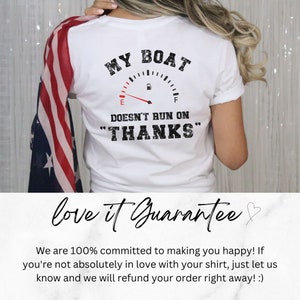 May include: White t-shirt with a graphic of a gas gauge that reads "MY BOAT DOESN'T RUN ON "THANKS"". The shirt is being worn by a person with a red, white, and blue scarf.