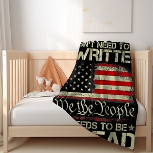 May include: A black and red throw blanket with a distressed American flag design. The text "We the People" is printed in white on the blanket, along with the phrase "Don't need to write it, it needs to be read."