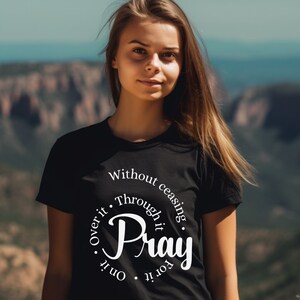 May include: Black t-shirt with a white circle graphic that says "Pray" with the words "Without ceasing", "Through it", "For it", "On it", and "Over it" surrounding the word "Pray".