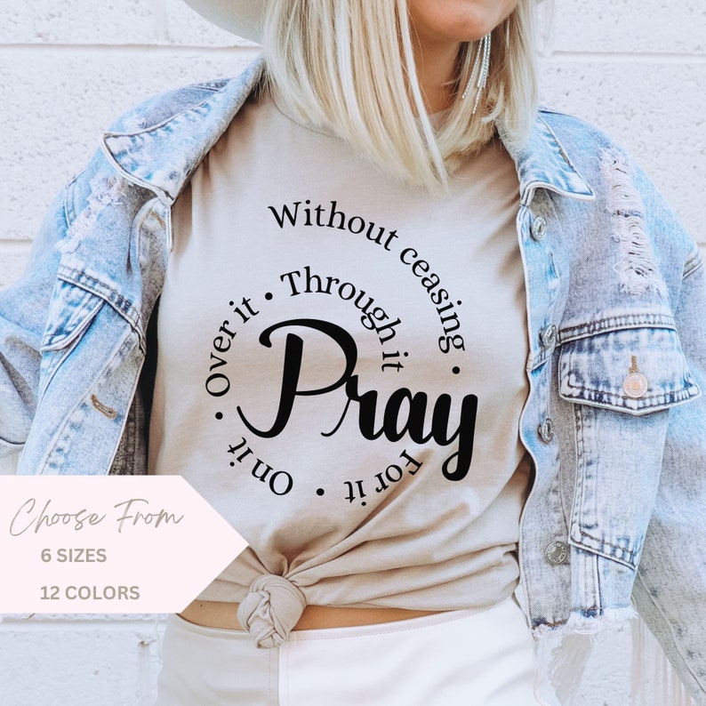 May include: A beige t-shirt with a black circle graphic that says "Pray" with the words "Without ceasing, Through it, Over it, On it, For it" surrounding the word "Pray".