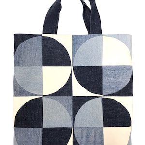 May include: A denim tote bag with a geometric pattern of white and blue circles. The bag has two denim handles.