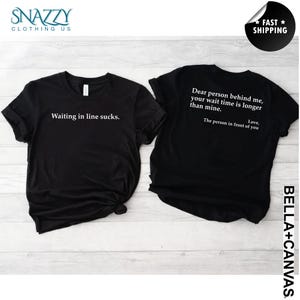 May include: Two black t-shirts with white text. One shirt says "Waiting in line sucks." The other says "Dear person behind me, your wait time is longer than mine. Love, The person in front of you."