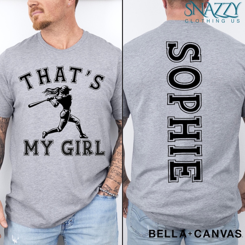 May include: Gray t-shirt with a baseball player graphic and the text "That's My Girl". The back of the shirt has the name "Sophie" printed vertically in a varsity style font.