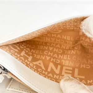 May include: Close-up of a white leather wallet interior. The interior lining is tan and features the repeating text "CHANEL". The wallet is open, revealing the interior design and the brand's logo.