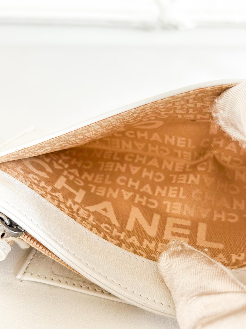 May include: Close-up of a white leather wallet interior. The interior lining is tan and features the repeating text "CHANEL". The wallet is open, revealing the interior design and the brand's logo.