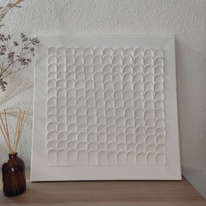 Op de afbeelding: Witte canvas wandkunst met een textuurpatroon van verhoogde, afgeronde vormen in een repeterend raster.