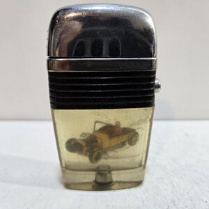 May include: A vintage lighter with a clear plastic body and a chrome top. The lighter features a printed image of a yellow hot rod car inside the plastic body.