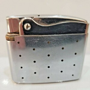 May include: A vintage silver-toned lighter with a hinged lid and a textured body. The lighter features a black accent on the top and a small, gold-colored wheel. Small circular holes are evenly spaced across the front.