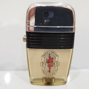 May include: A vintage silver and black lighter with a clear plastic window showing a logo that says "Shield of Quality Powers Roofing & Siding Co."