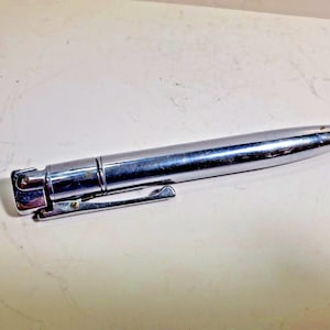 May include: A silver-toned lighter shaped like a pencil. The lighter has a retractable tip and a built-in flint.