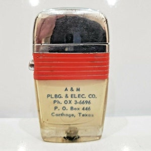 May include: A vintage lighter with a red and white striped band and a white label that reads "A & M PLBG. & ELEC. CO. Ph. OX 3-6696 P. O. Box 446 Carthage, Texas".
