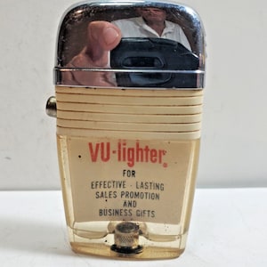 May include: A white and chrome lighter with the text "VU-lighter" in red. The lighter has the text "For Effective Lasting Sales Promotion and Business Gifts" printed on it.