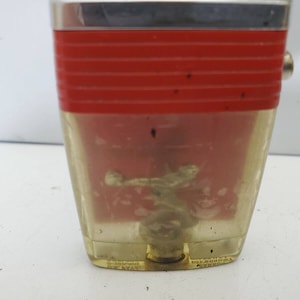 May include: A vintage lighter with a red and silver design. The lighter is clear and shows a design inside. The lighter has a small hole on the side.