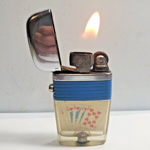 May include: A blue and silver lighter with a clear plastic body. The lighter has a design of playing cards on the front. The lighter is lit and the flame is visible.