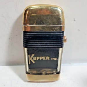 May include: A gold and black lighter with the text "KUPPER INC." on the front.
