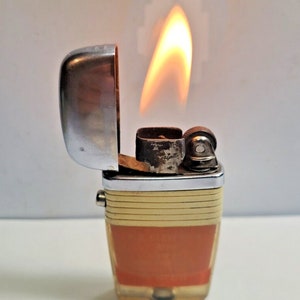 May include: A vintage lighter with a white and orange plastic body and a silver top. The lighter is open and the flame is lit.