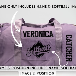 May include: A lavender duffel bag with a black "VERONICA" text and a "Softball" logo. The word "CATCHER" is printed vertically on the side. The bag has a top handle and a front pocket.