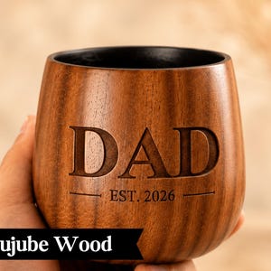 A wooden mug with the word "DAD" engraved on it, along with the year "EST. 2026" below it.