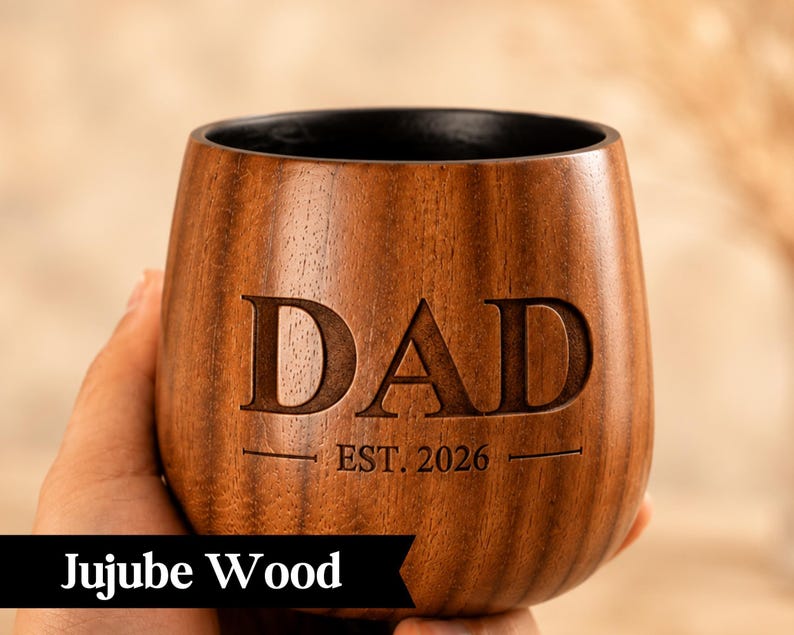 A wooden mug with the word "DAD" engraved on it, along with the year "EST. 2026" below it.