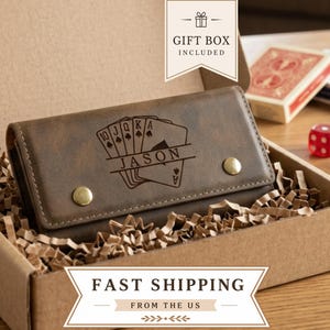 May include: A brown leather wallet featuring an engraved design of a royal flush poker hand with the name JASON centered across the cards. The wallet has two gold-toned metal snap buttons and is presented inside a cardboard gift box with paper filler.