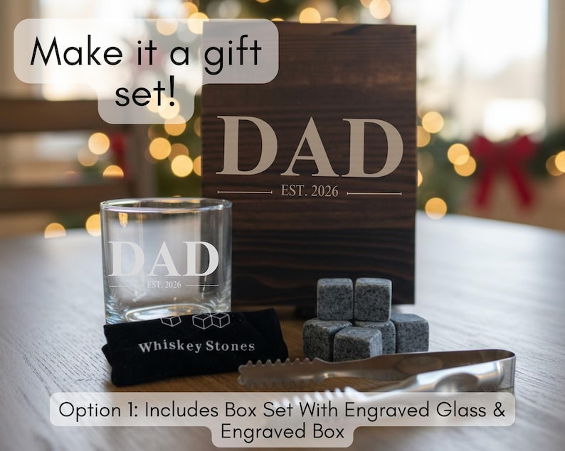 a gift set that includes a wooden box with the word "DAD" engraved on it, a glass, and whiskey stones. The text on the image suggests that the gift set can be customized with an engraved glass and a carved wooden box.