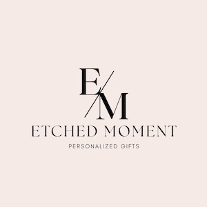 May include: Logo for "Etched Moment" featuring stylized black letters "E" and "M" with a diagonal line. Below the letters is the text "ETCHED MOMENT" and "PERSONALIZED GIFTS" in a serif font, all on a light pink background.