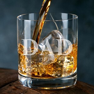 A glass of amber-colored liquid, likely whiskey, with ice cubes, and a golden-colored object being poured into the glass.