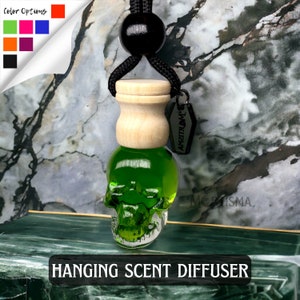May include: Green glass skull hanging car air freshener with a wooden lid and a black cord. The tag on the cord reads "MORBIDLY", and the skull is filled with green liquid.