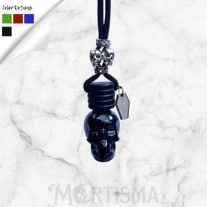 May include: A black skull-shaped car air freshener with a silver skull accent and a small tag. The air freshener is suspended by a black cord. The text "Mortisma" is at the bottom of the image.