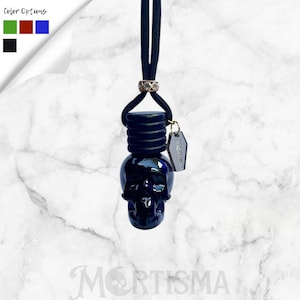 May include: A black skull-shaped car air freshener with a black cord and a small tag. The air freshener has a dark blue hue and a gold-colored ring. The word "MORTISMA" is printed at the bottom of the image.