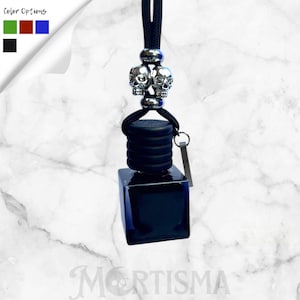 May include: A black car air freshener with a silver skull charm. The air freshener has a black square bottle and a black cap. The top of the air freshener has a silver charm with two skulls. The text "Color Options" is in the top left corner.
