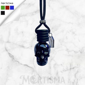 May include: A black skull-shaped car air freshener with a black cord and a small tag that reads "AM21XLOVE". The air freshener has a glossy finish and is hanging against a marble background. Color options are shown in the upper left.